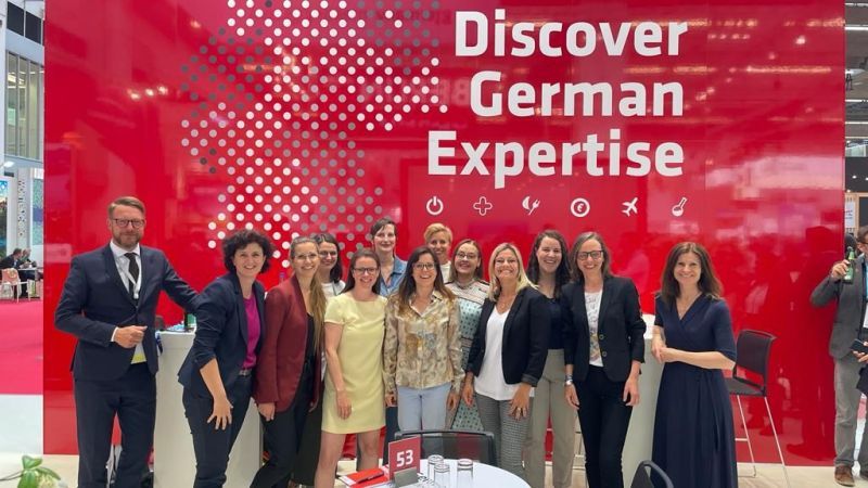 Foto mit einigen Teilnehmerinnen der IMEX Coffeebreak vor der roten Messewand des GCB. Zu sehen ist darauf ein großer Schriftzug mit "Discover German Expertise"